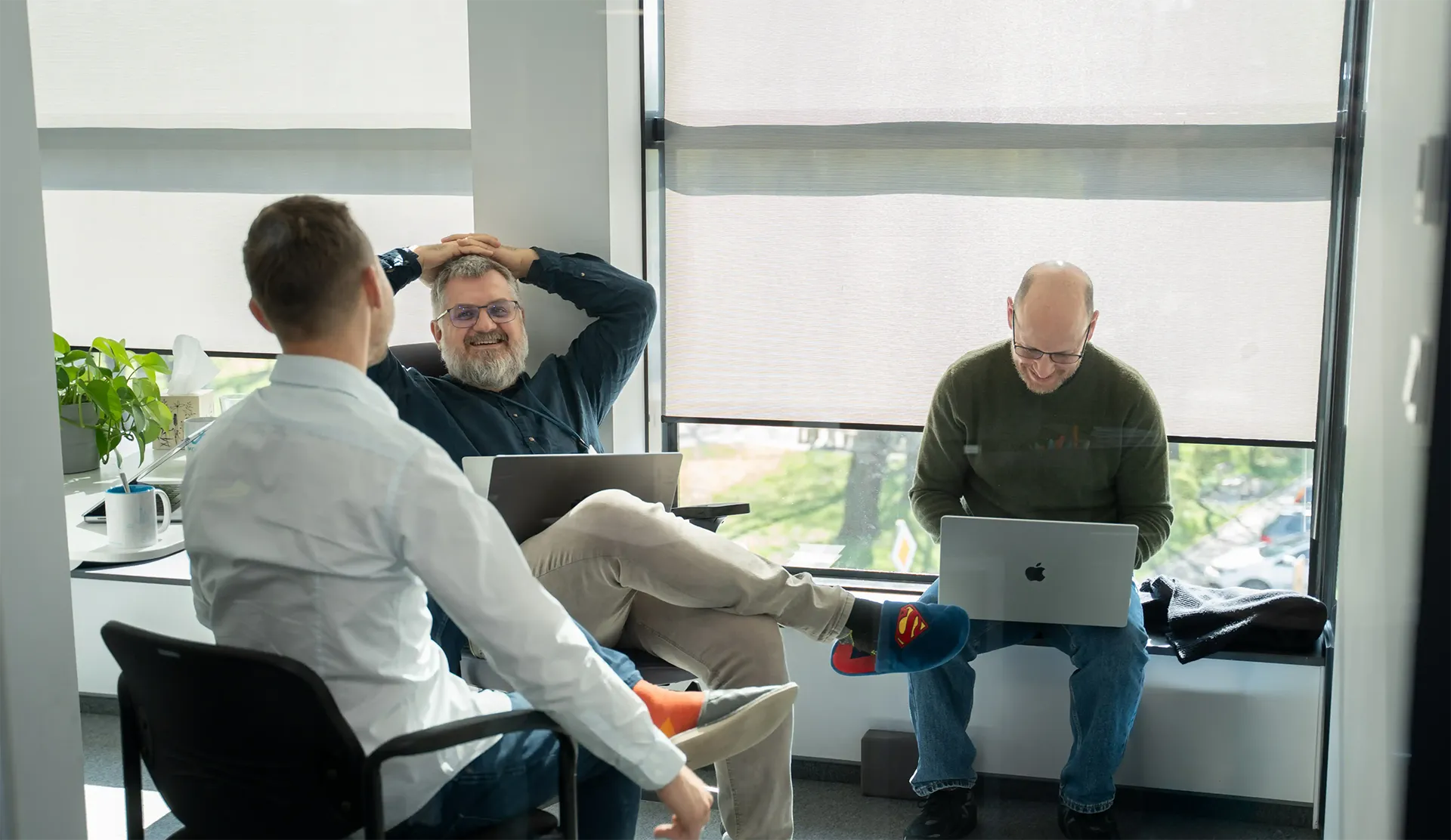 Three men sit in an office space with laptops.