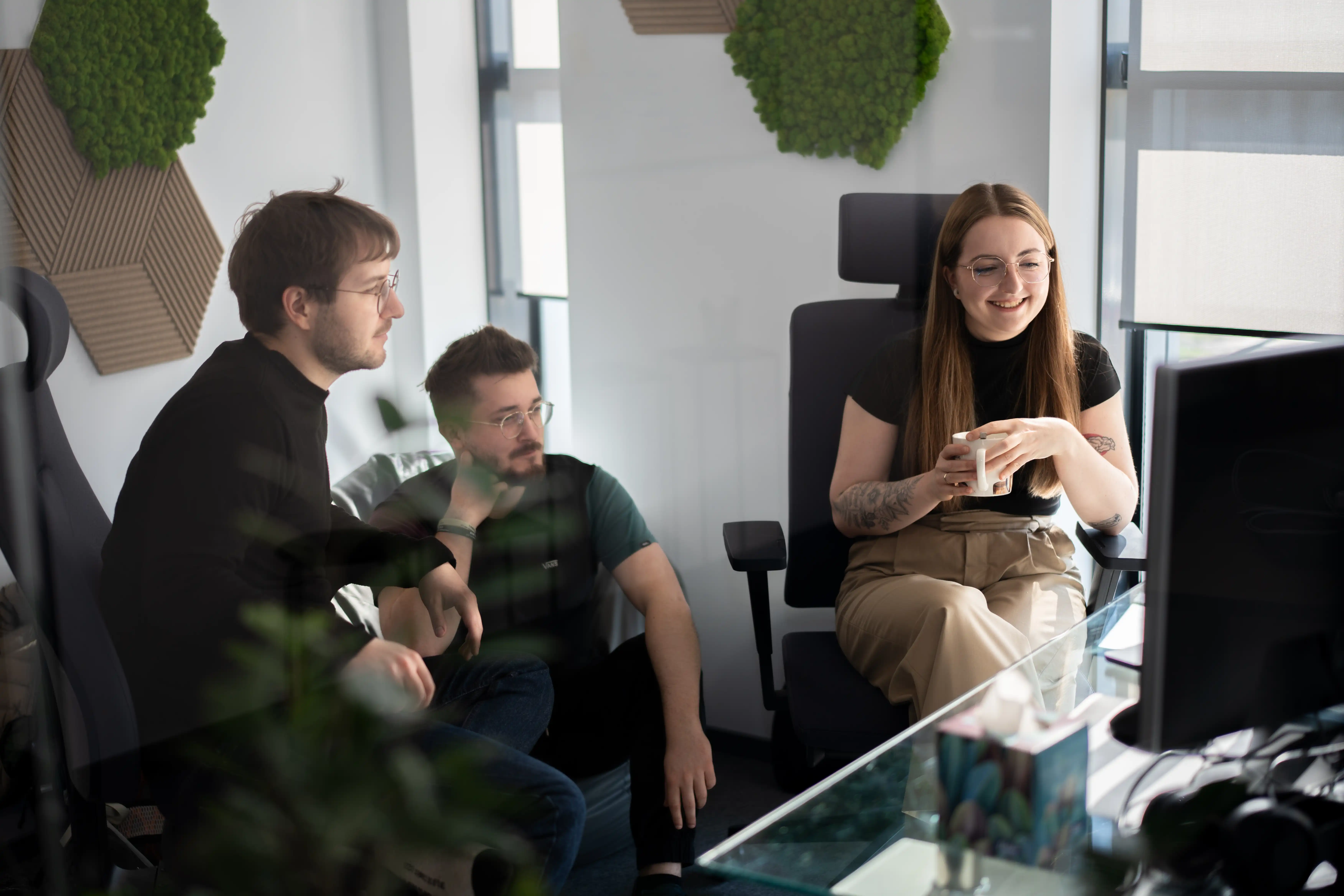 Three people sit and talk in a modern office.