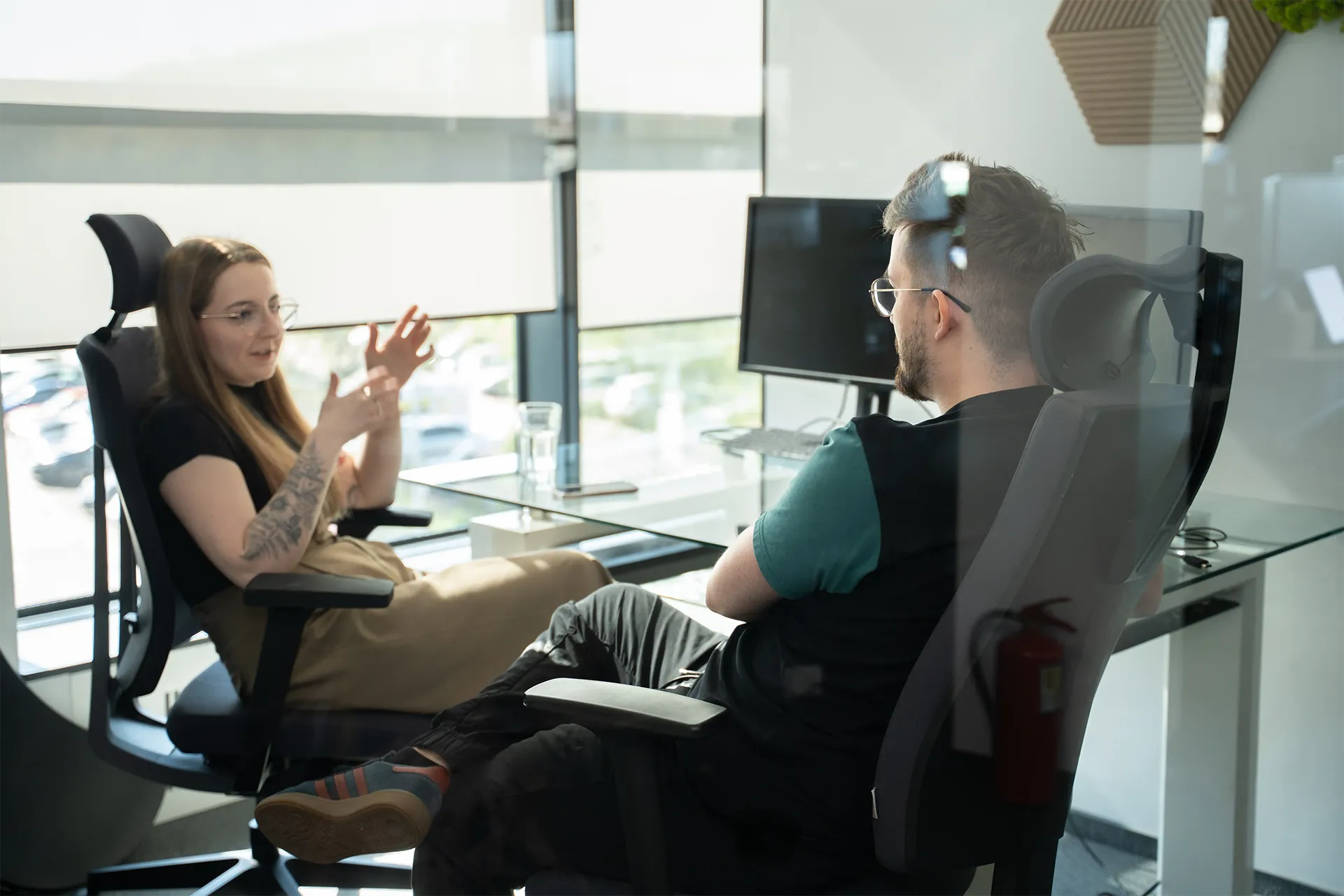 Two people sit in office chairs.